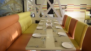 Ein Restaurant mit einem langen Esstisch, bequemen Sitzgelegenheiten und einer farbenfrohen Wandgestaltung.