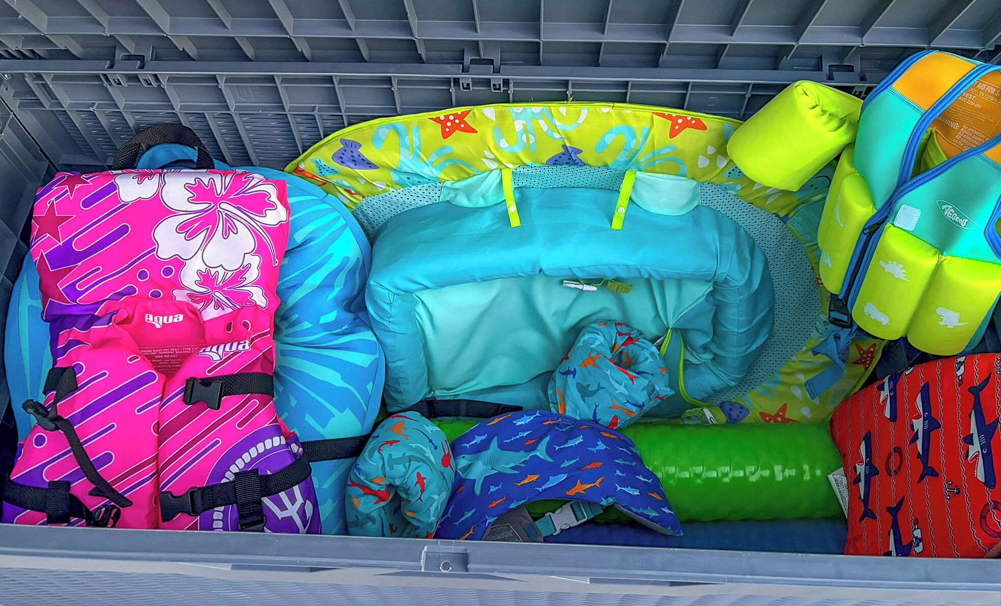 A storage area with various colorful bags and items, including a pink bag with a star pattern, a blue bag with shark prints, and a green bag with a dolphin design.