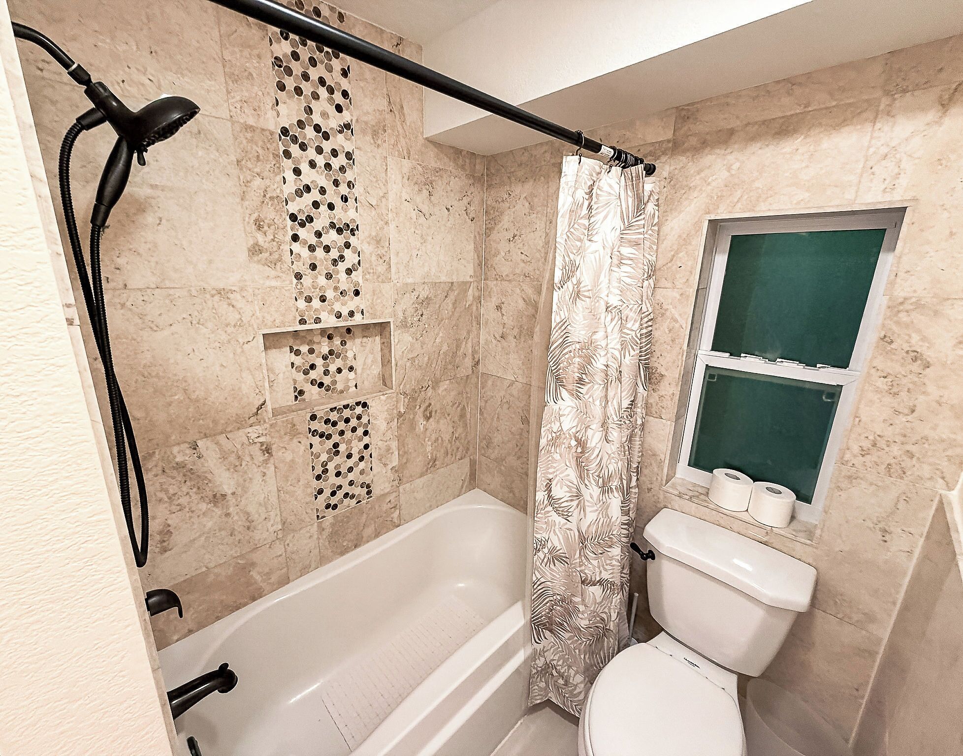 A bathroom with a bathtub, toilet, shower curtain, and a window.