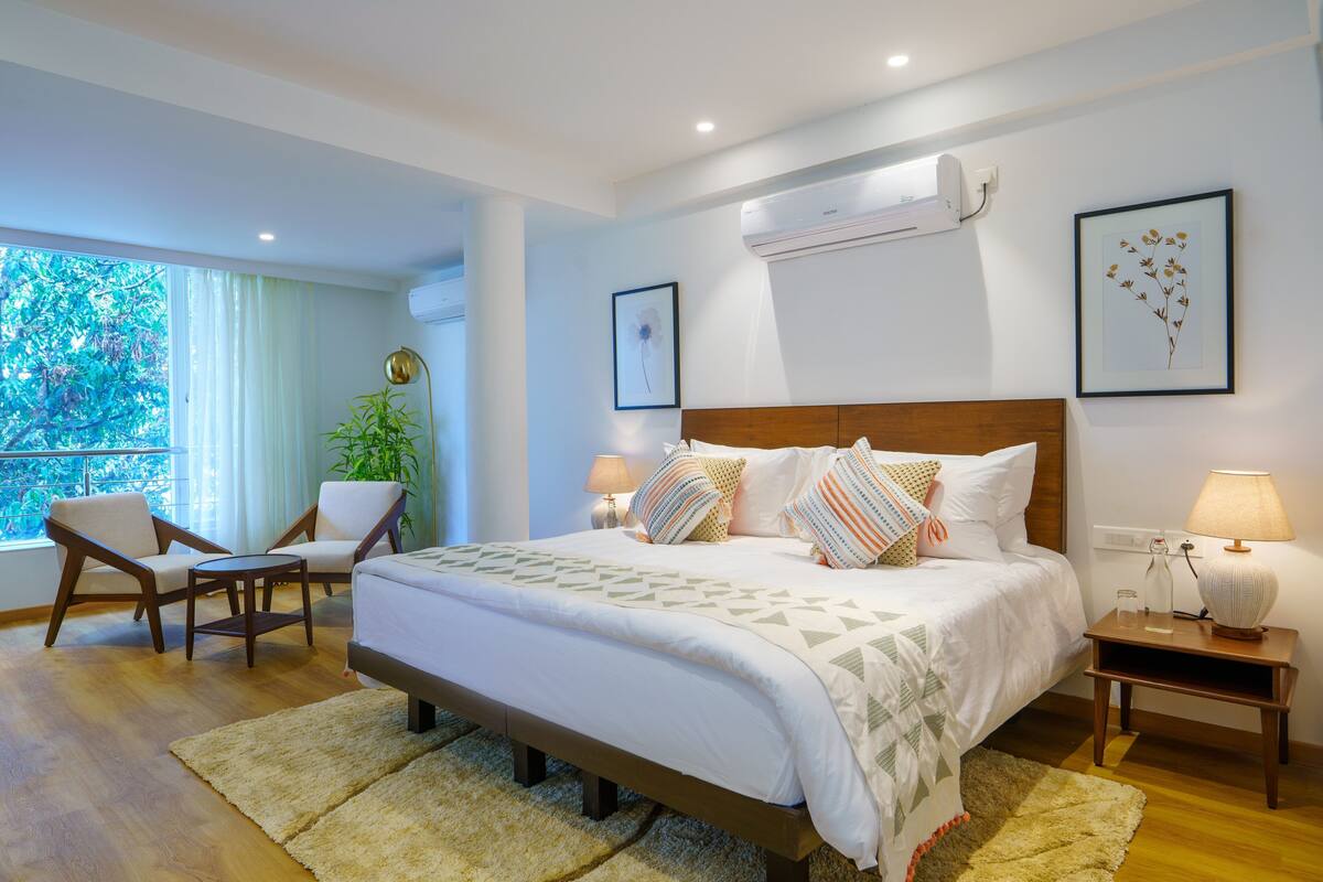 A bedroom with a bed, bedside tables, a chair, a potted plant, and a window with a view.