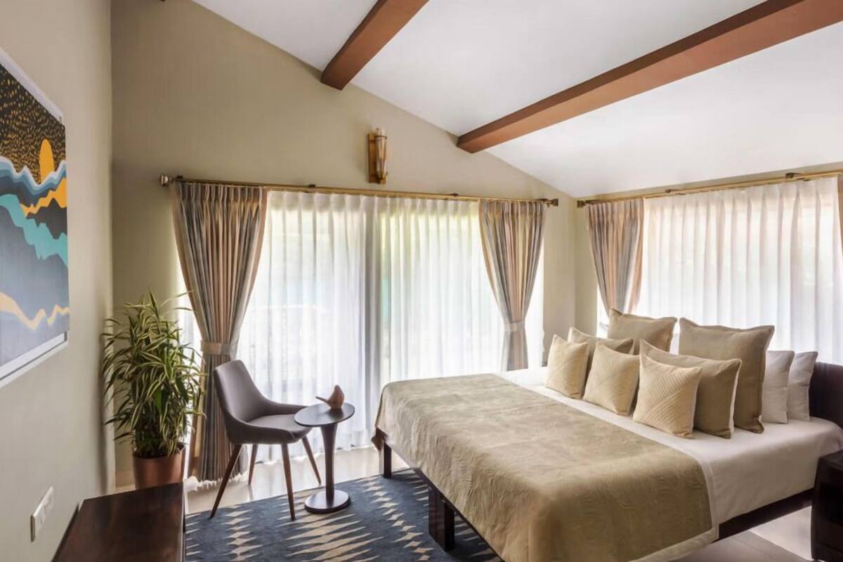 A bedroom with a bed, a chair, a small table, and a potted plant.