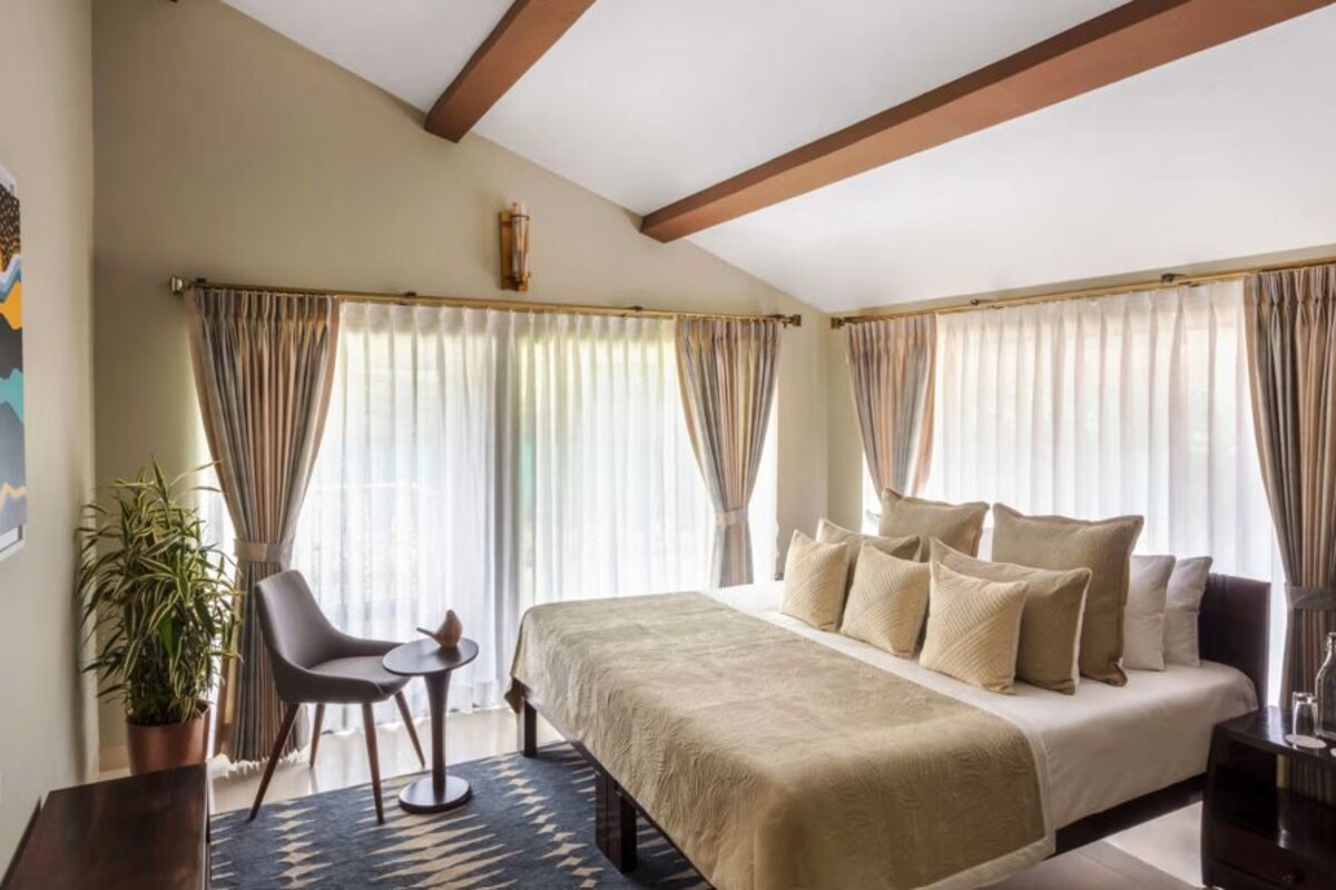 A bedroom with a bed, a chair, a small table, and a potted plant.