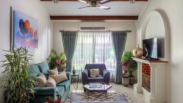 A living room with a sofa, armchair, coffee table, TV, ceiling fan, and potted plants. - Ama Stays & Trails Sluice House, Lonavala (Mawal)
