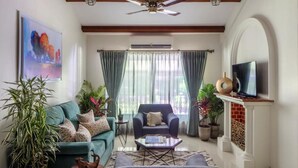 A living room with a sofa, armchair, coffee table, TV, ceiling fan, and potted plants. - Ama Stays & Trails Sluice House, Lonavala (Mawal)