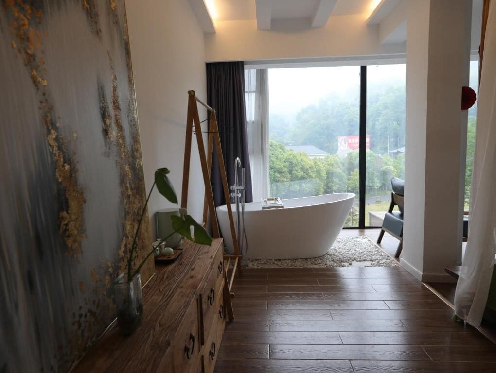Un baño moderno con una bañera independiente, un tocador de madera y un ventanal con vistas a la vegetación.