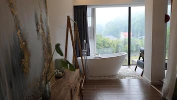 Un baño moderno con una bañera independiente, un tocador de madera y un ventanal con vistas a la vegetación.