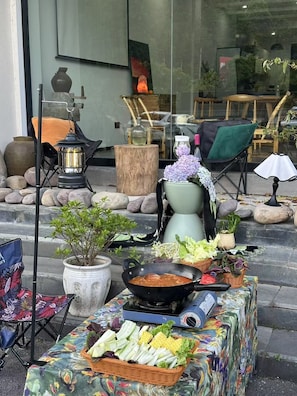 Un área de estar al aire libre con una mesa dispuesta con verduras, una estufa portátil y varias macetas.
