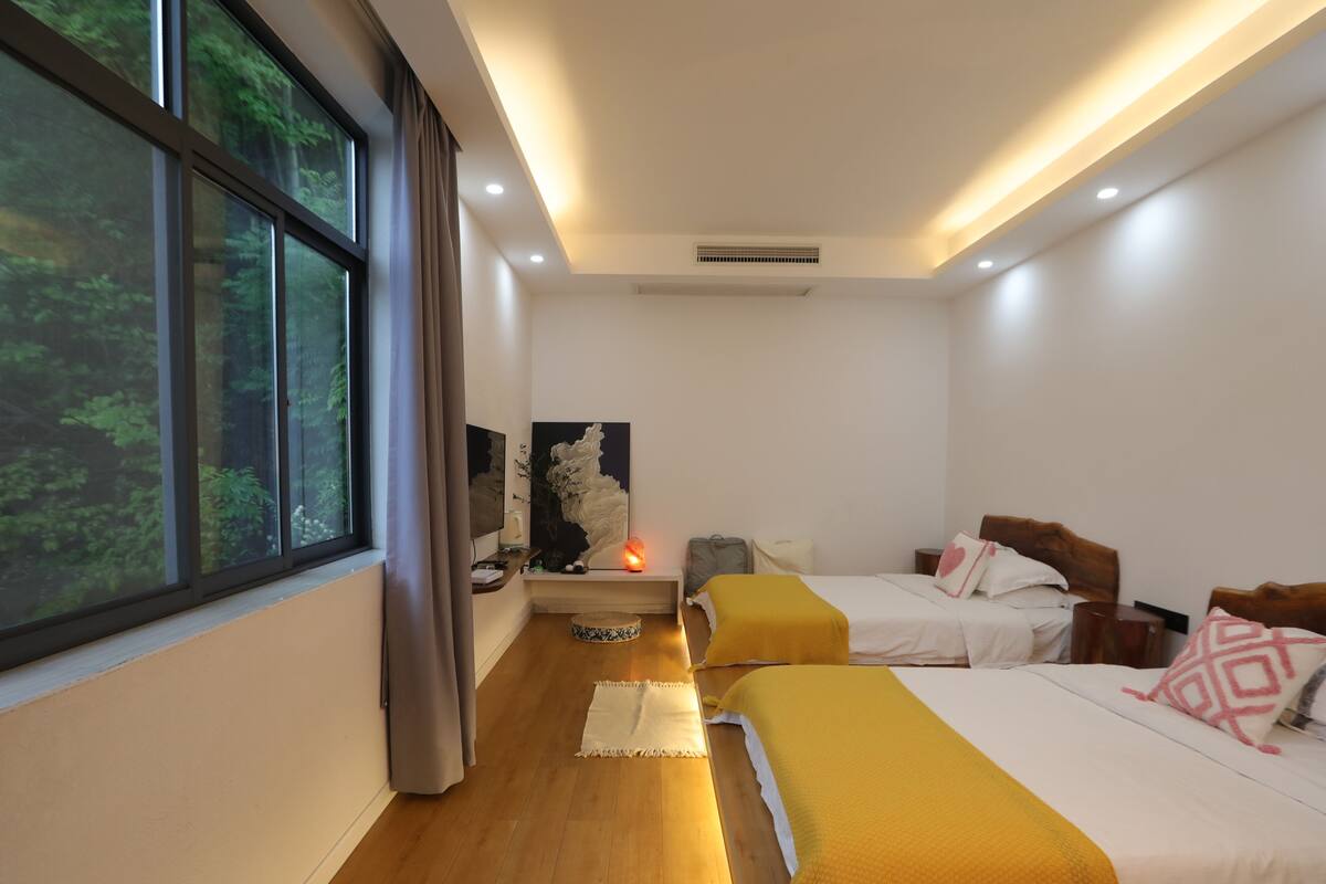 Habitación de hotel con dos camas, una ventana con cortinas, una mesita de noche, una lámpara y una obra de arte colgada en la pared.