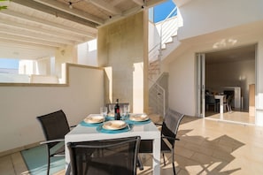 A dining area with a table set for four, chairs, a bottle of wine, and a staircase leading to an upper level.