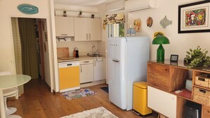 A compact kitchen with a dishwasher, a refrigerator, and a sink. There is a small dining table with chairs, a patterned rug, and a wooden cabinet with a green plant. - Exceptional garden level pool cap d'antibes (Antibes)
