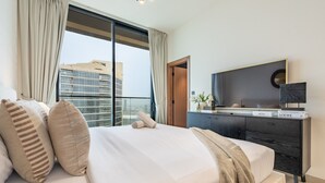 Ein modernes Hotelzimmer mit einem großen Bett, einem Flachbildfernseher, einem Schreibtisch mit Computer und Blick auf die Stadtlandschaft.