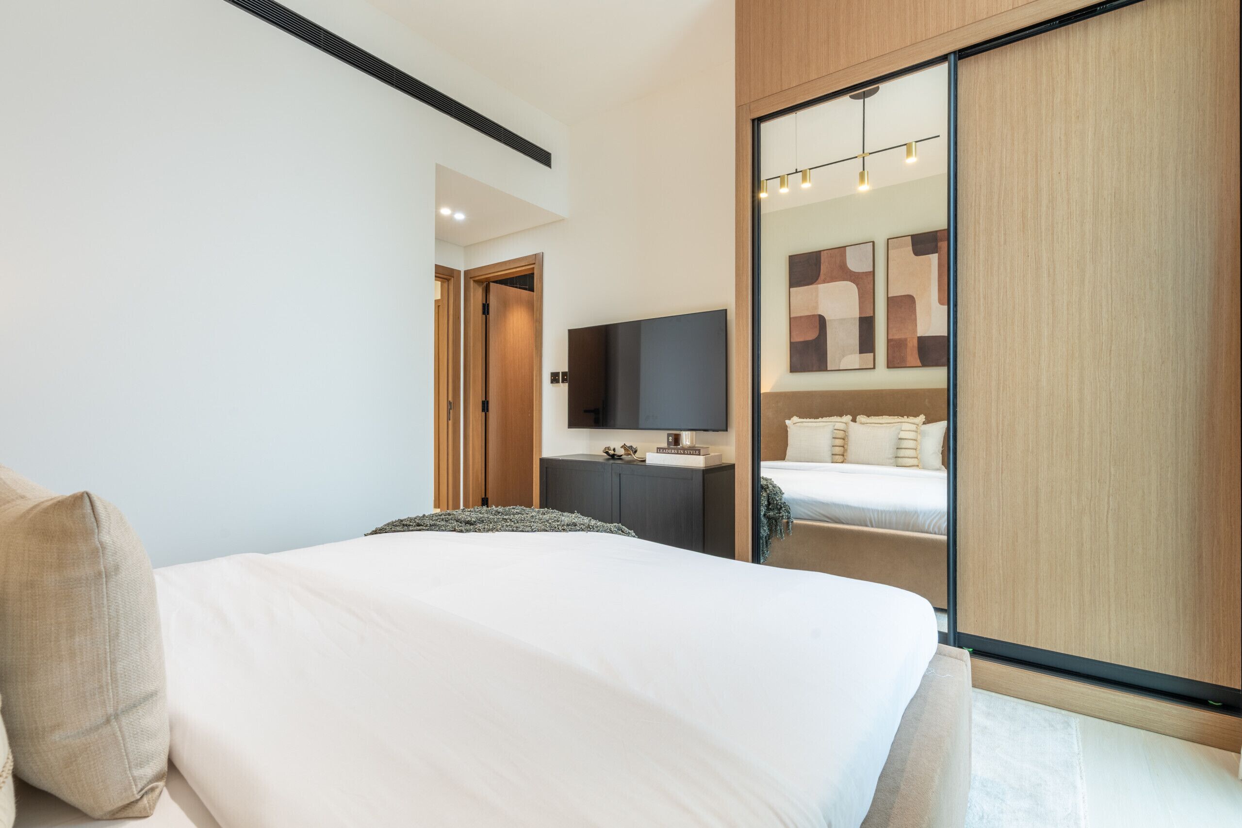 A modern hotel room with a large bed, a flat-screen TV, a desk, and a wardrobe.