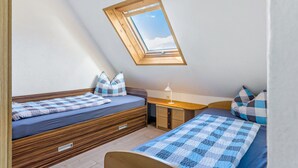 A bedroom with a skylight, two beds, a desk, and a small cabinet.