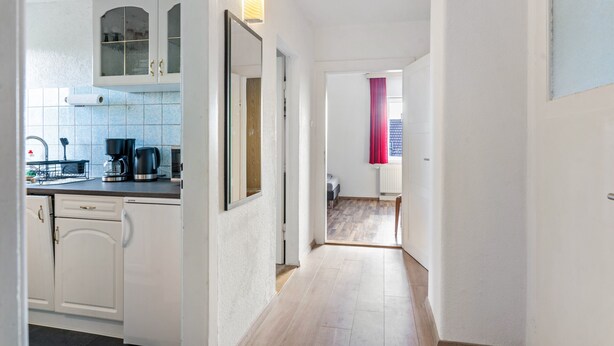A kitchen with white cabinets, a coffee maker, and a window with a red curtain.