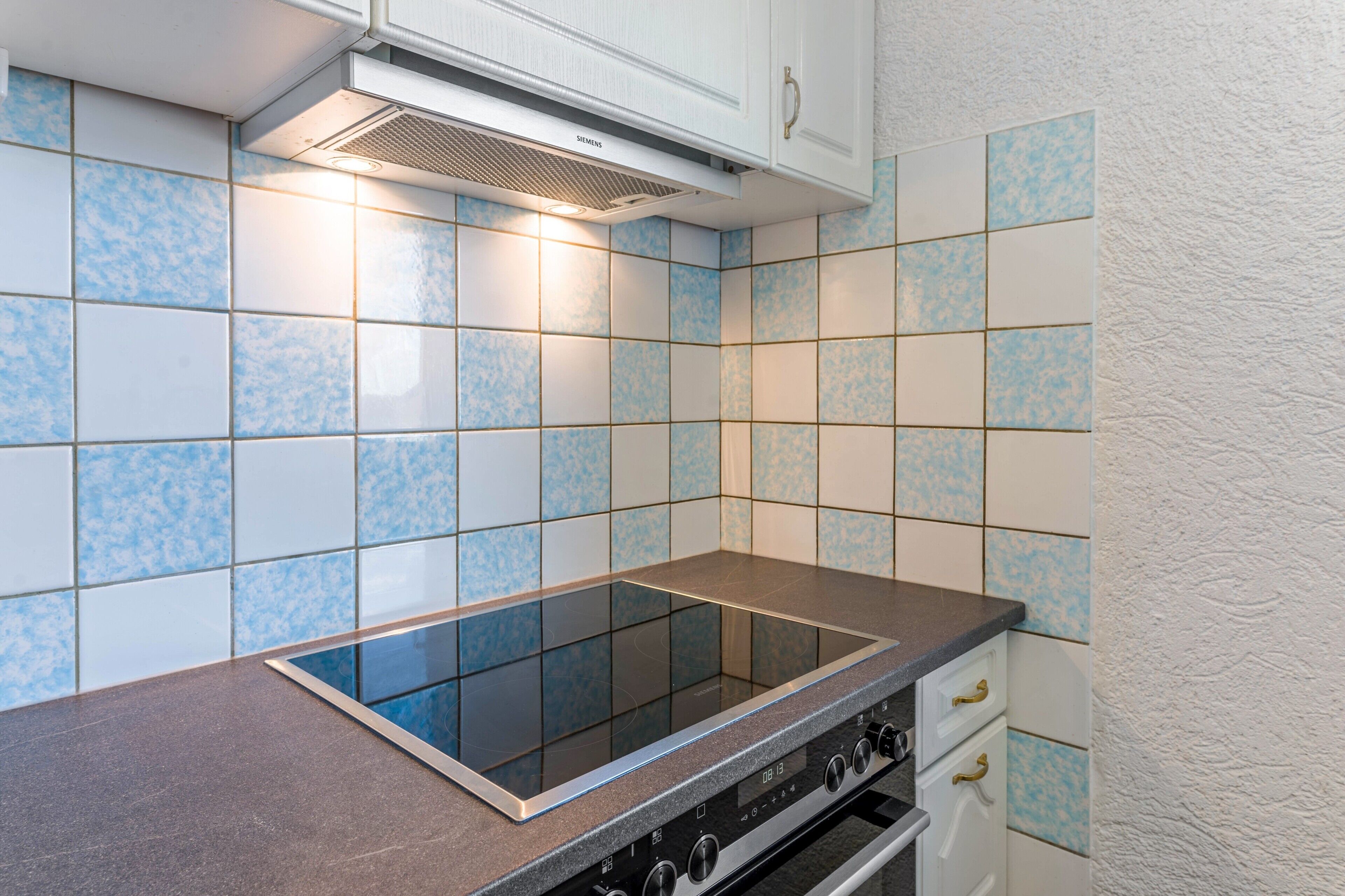 Una cocina con cocina por inducción negra, armarios blancos y azulejos con diseño azul.