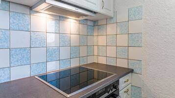Una cocina con cocina por inducción negra, armarios blancos y azulejos con diseño azul.