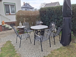 An outdoor patio with a round table and chairs, a statue, and a hedge.