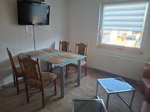 A dining area with a table, chairs, a television, and a window with blinds.