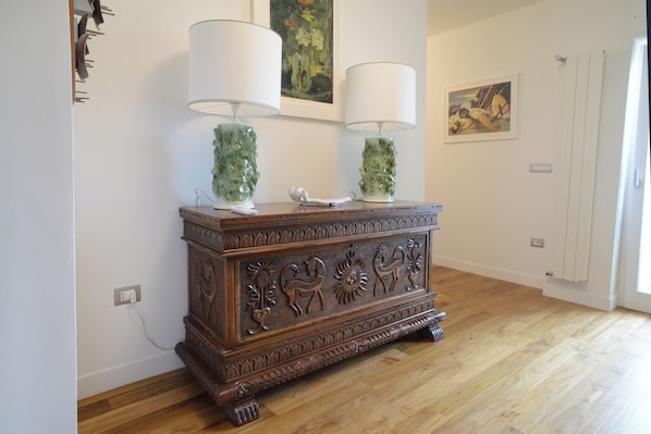 A wooden cabinet with two lamps, a painting, and a door in a room with wooden flooring.