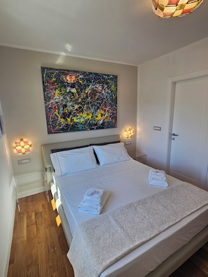 Una habitación de hotel con una cama grande, un cuadro abstracto colgado en la pared, lámparas de noche y una puerta.