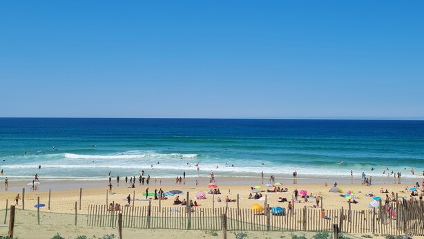 Een strand met mensen, parasols en een houten hek.