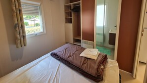 Een slaapkamer met een bed, een raam met gordijnen, een kledingkast en een spiegel.
