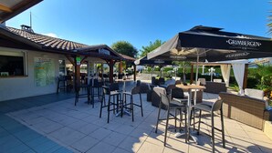 Een terras met tafels en stoelen, parasols en een overdekt zitgedeelte.