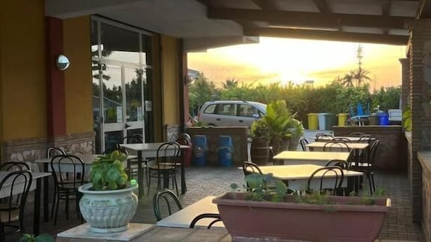 Un patio al aire libre con mesas y sillas, plantas en macetas y vista al atardecer.