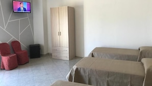 Una habitación con televisión, armario, dos camas y una silla roja con estampado.