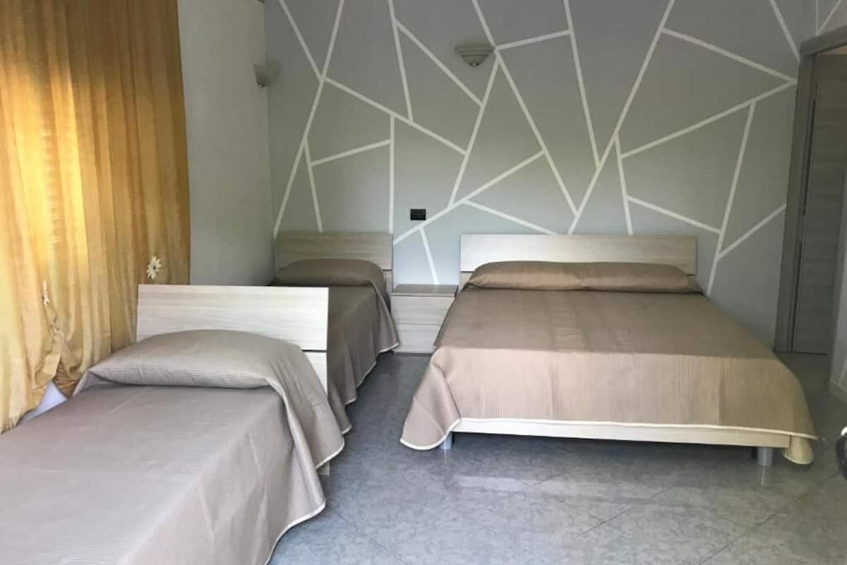 Une chambre avec deux lits, une tête de lit en bois, un mur de couleur claire orné d’un motif géométrique et un sol carrelé.