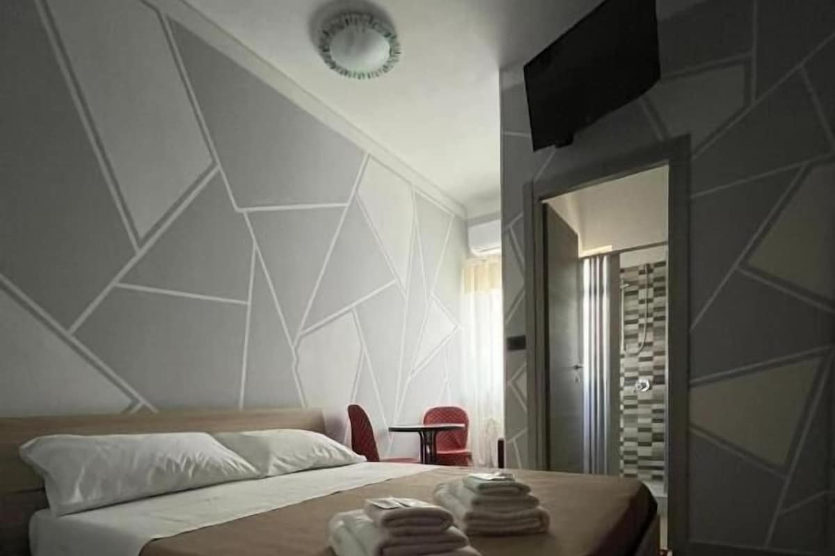 Habitación de hotel con una cama, un televisor de pantalla plana montado en la pared y vista al baño a través de una puerta abierta.