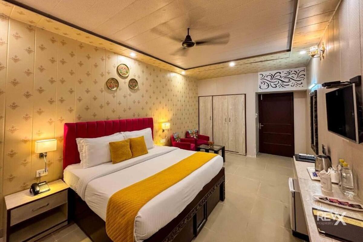 Habitación de hotel con cama, mesita de noche, lámpara, televisor, armario y ventilador de techo.