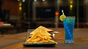 A table with a grilled sandwich, fries, and a blue drink with a lemon slice and striped straw. - The Shanti Naturecure on Ganga (Rishikesh)