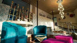 A room with a wooden ceiling, a staircase, a blue armchair, a round table, and a pink ottoman.