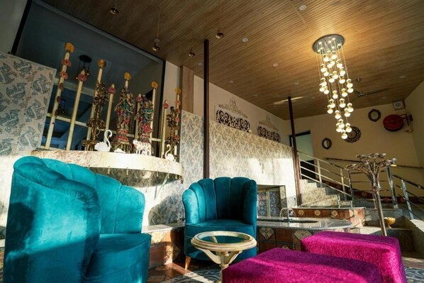 A room with a wooden ceiling, a staircase, a blue armchair, a round table, and a pink ottoman.