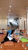A group of people stretching on mats in a spacious room with a high ceiling and a staircase in the background.