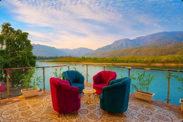 A terrace with a view of a river and mountains, furnished with colorful chairs and a small table. - The Shanti Naturecure on Ganga (Rishikesh)