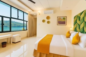 A hotel room with a large window, a bed with a green headboard, and a desk with a chair.