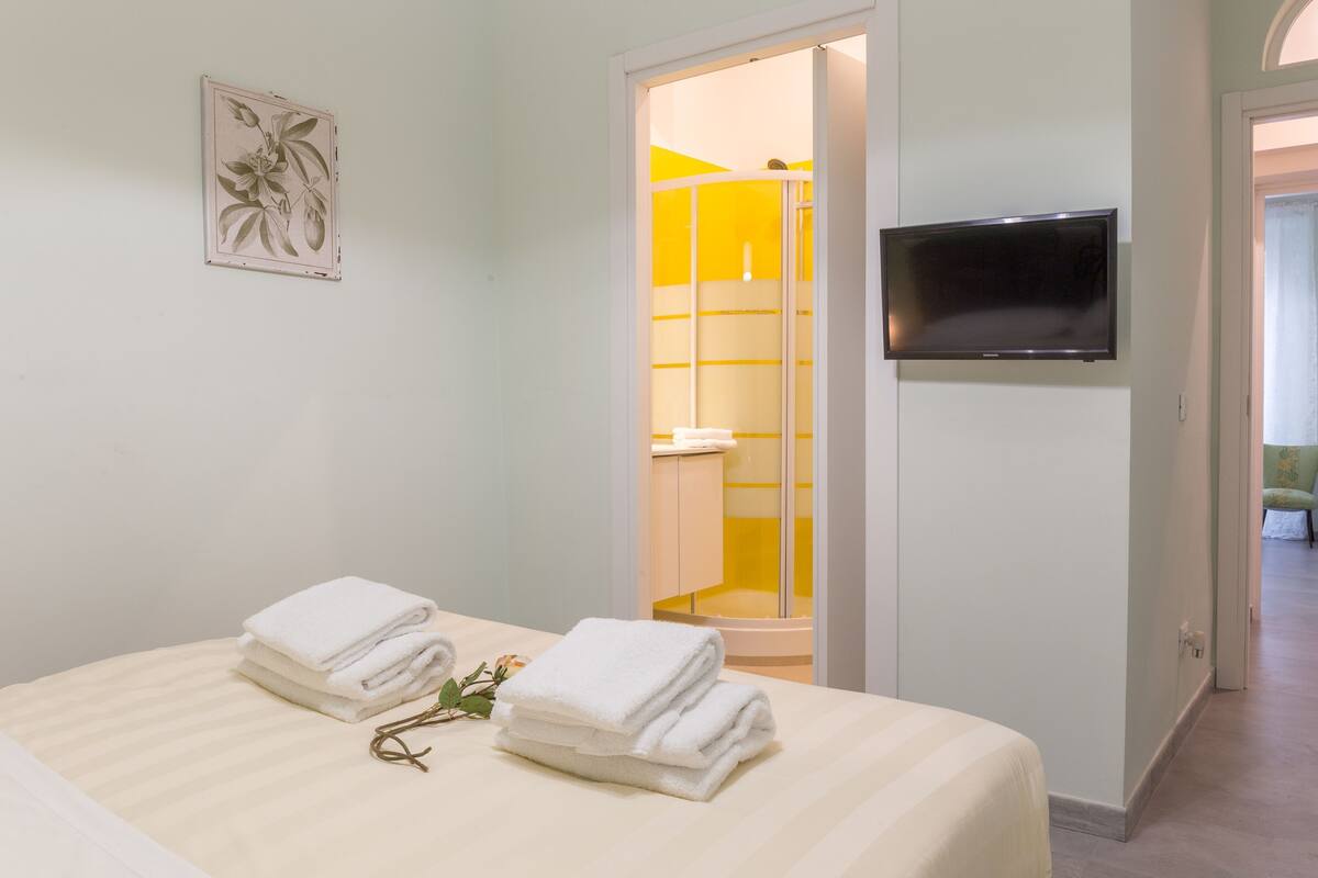 Une chambre d’hôtel avec un lit, une télévision et une salle de bain dotée d’une douche jaune, ainsi qu’une porte donnant sur une autre chambre.