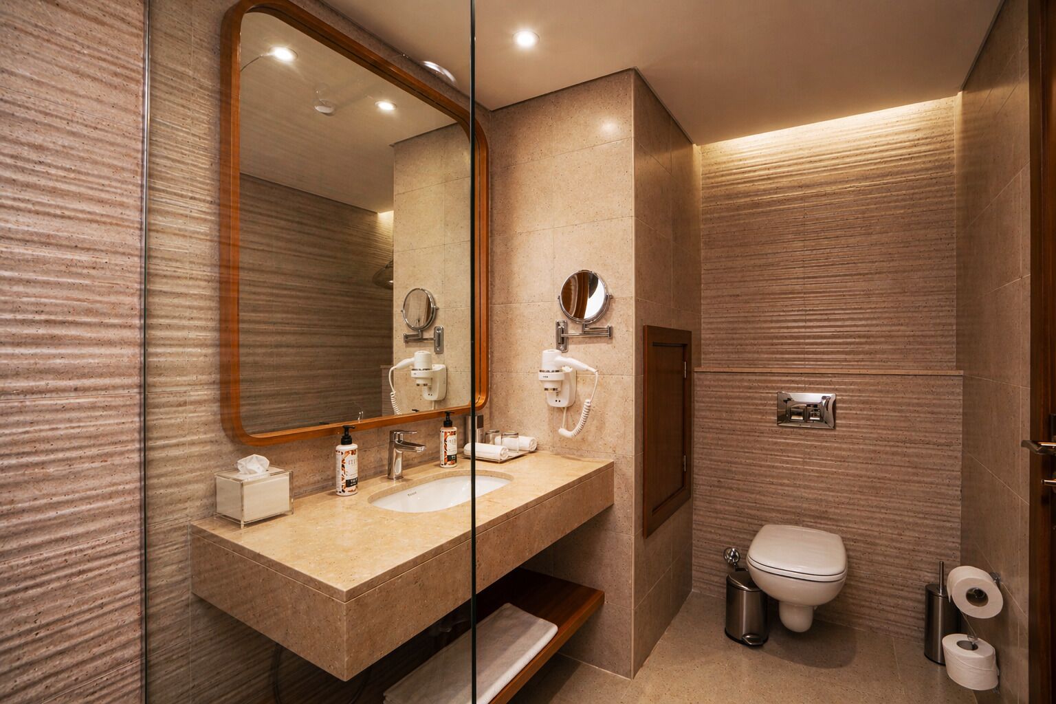 A modern bathroom with a large mirror, two sinks, a toilet, and a shower area.