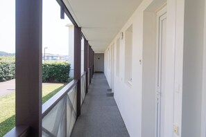 Ein Korridor mit Balkon, weißen Wänden und Blick auf Grünflächen und Gebäude.