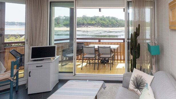 Una habitación con televisión, escritorio, silla, sofá y vista a la playa.