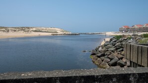 Escena costera con un mar tranquilo, una playa arenosa y un edificio con tejados rojos.
