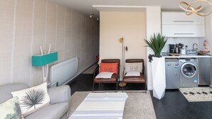 Una sala moderna con un sofá, una mesa de centro, una lavadora y un comedor con sillas.