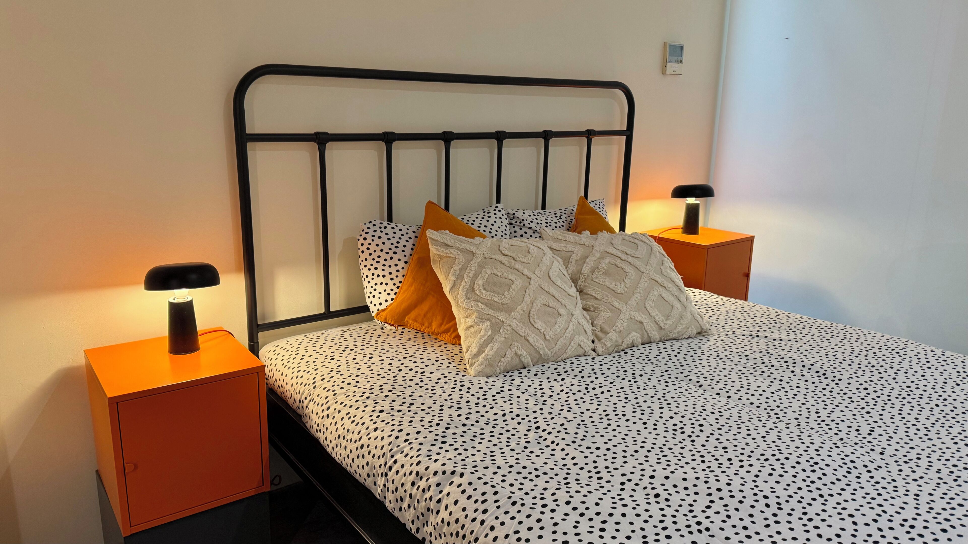 A bed with a metal headboard, two nightstands with lamps, and a polka dot bedspread.