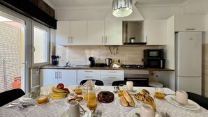 Ett modernt kök med vita skåp, ett matbord dukat för frukost och utsikt över omgivningen.