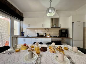 Eine moderne Küche mit weißen Schränken, einem für das Frühstück gedeckten Tisch und Blick ins Freie.
