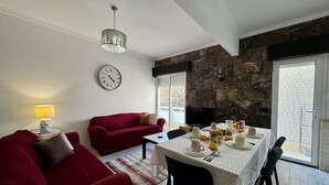 Ett vardagsrum med en röd soffa, ett matbord dukat med frukostmat, en klocka på väggen och en vägg av sten.