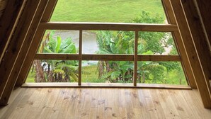 A room with a sloped wooden ceiling and a large window offering a view of a green landscape. - Paraitinga Glamping  (São Luiz do Paraitinga)