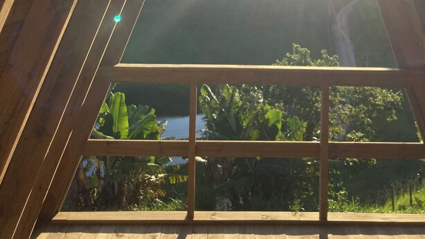 A wooden structure with a triangular window framing a view of a landscape with mountains and vegetation. - Paraitinga Glamping  (São Luiz do Paraitinga)